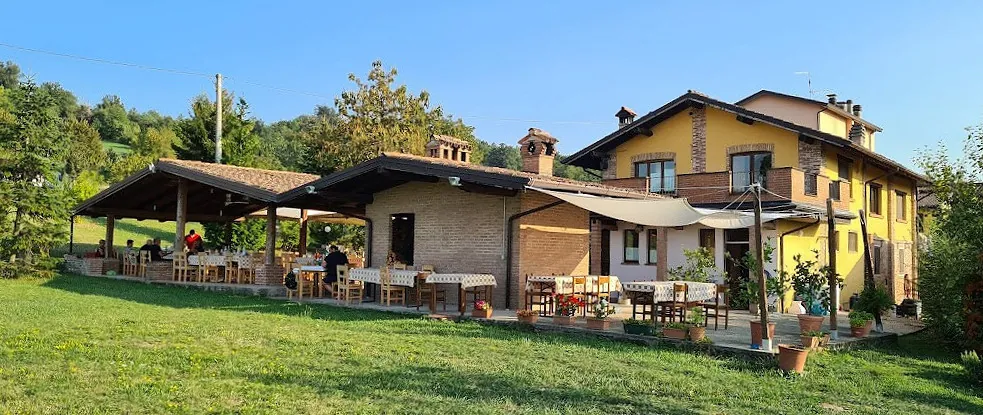 L'agriturismo La Pattona visto dal prato: la casa gialla, il portico con i tavoli apparecchiati e la tenda da sole.