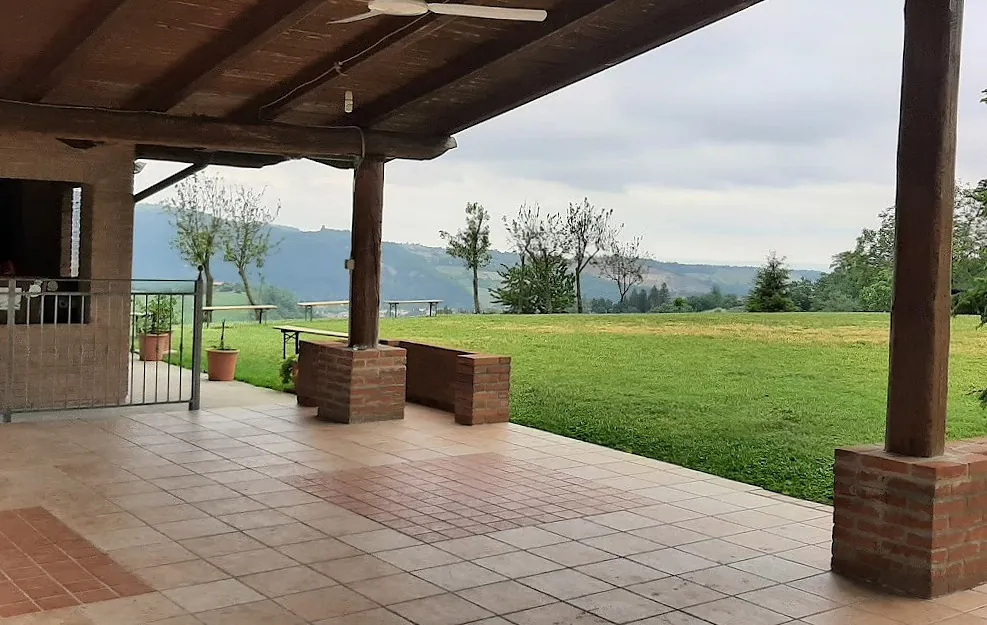 La vista dal portico: pali in legno, pilastri in mattoni, il prato e le colline.
