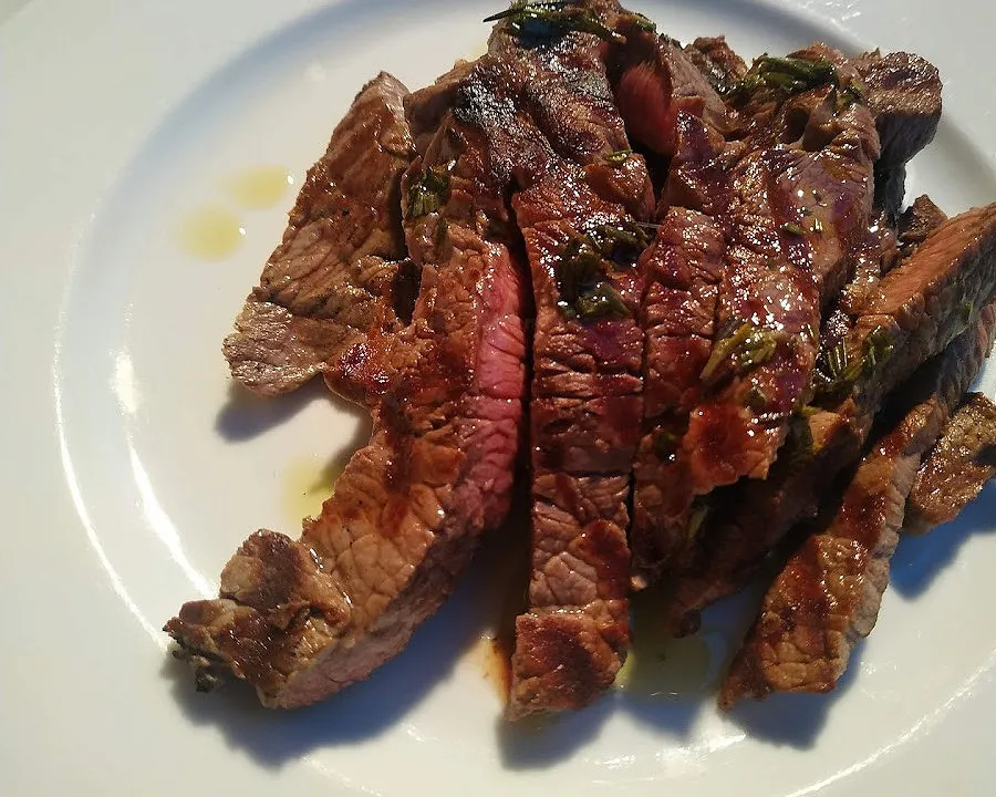 Tagliata di manzo appena tagliata, con rosmarino e un filo d'olio.