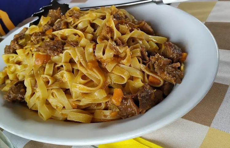 Un piatto fondo di tagliatelle al ragù su una tovaglia a quadretti gialli.
