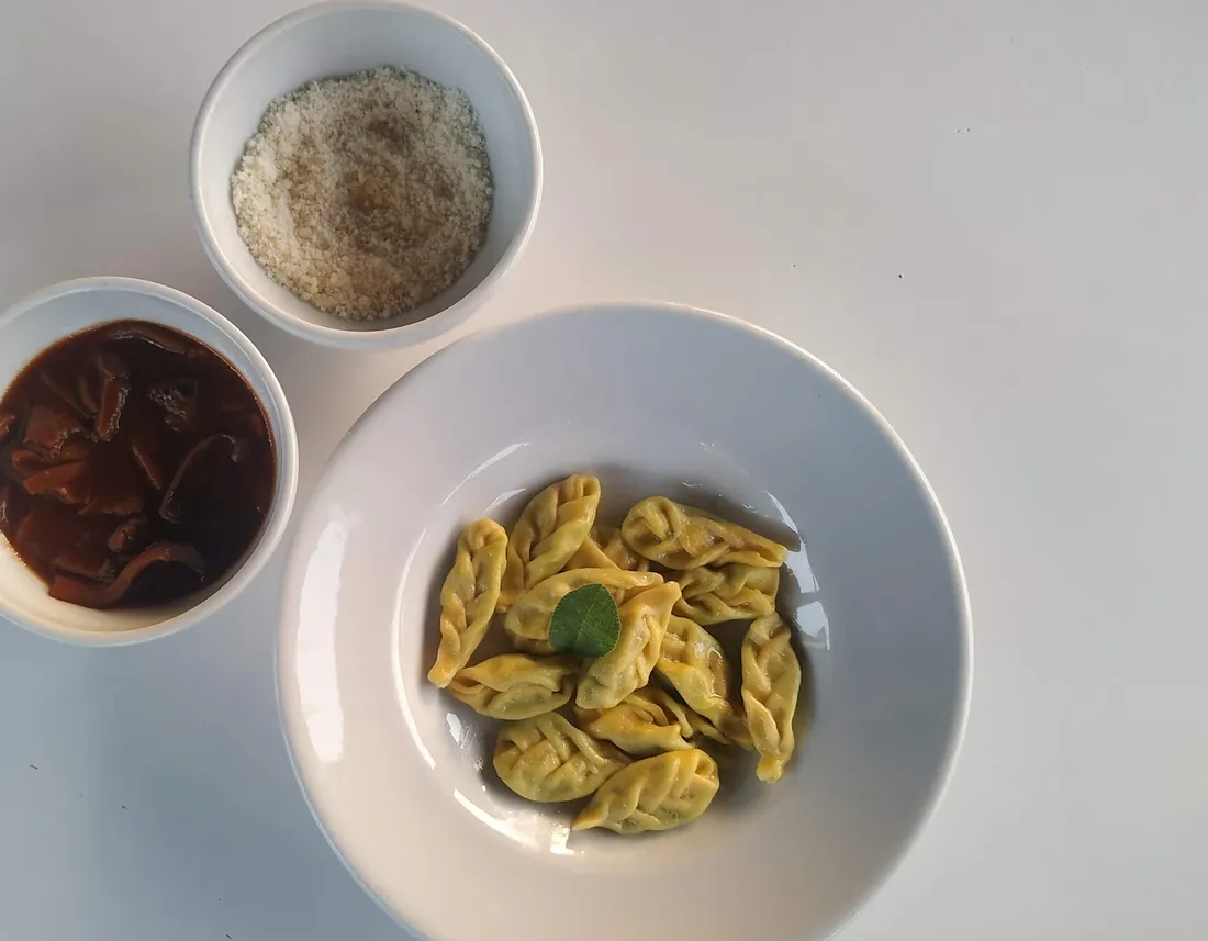 Tortelli piacentini con il sugo di funghi e il formaggio grattugiato a parte.
